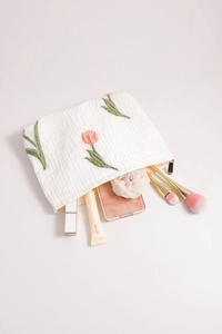 Detailed view of tulip floral embroidery on white wrinkled fabric makeup bag with brushes