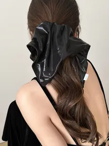Close-up of oversized black glossy satin scrunchie styled on a brunette ponytail