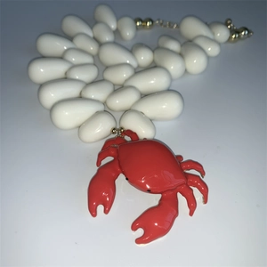 Detail of red crab pendant with large white teardrop beads and golden hardware