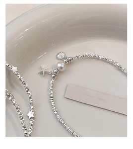 Macro view of silver star and seashell charms with a pearl on a minimalist beaded bracelet