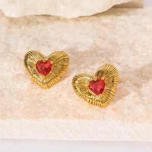 Macro detail of gold-plated heart earrings with red zircon and radiating texture