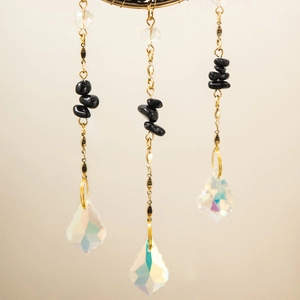 Detail of hanging suncatcher with gold metal chains, black stones and prism crystal pendants