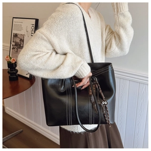 Detail of black leather tote bag featuring white contrast stitching and a cat charm accessory