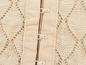 Macro detail of beige hollow knit fabric with white metal hook-and-eye closure