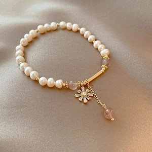 Macro shot of freshwater pearl bracelet with red gemstone and petal pendant on champagne silk