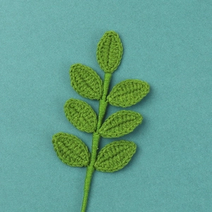Detailed macro view of a handmade green crochet stem with seven knitted leaves