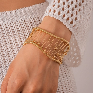 Détail d'un large bracelet manchette tissé doré avec perles porté au poignet
