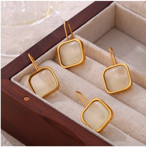 Macro detail of gold square drop earrings with resin stones in a wooden jewelry box