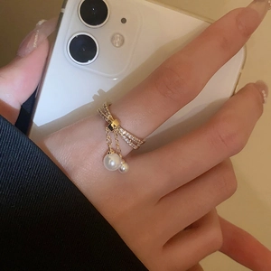Detail of gold-plated crossover ring with pavé zircon bow and hanging pearl tassels