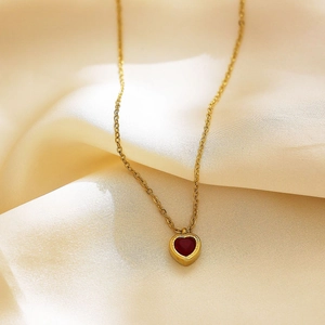 Detail of 18k gold plated necklace with heart shaped red zircon pendant on silk