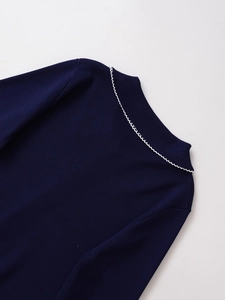 Detail eines dunkelblauen Strickpullovers mit weißer Wellenstickerei am Polokragen