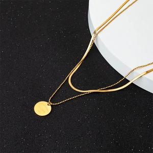 Macro shot of double layered gold snake chain and beaded necklace with round charm