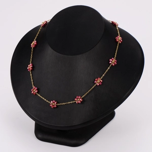 Elegant gold necklace with red crystal daisies displayed on a black velvet bust stand