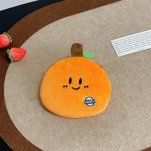 Detail of cute plush orange coin purse with happy embroidery and green leaf on wood tray