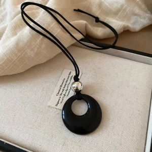 Detail of a minimalist black pendant on a cord necklace with a silver bead decoration
