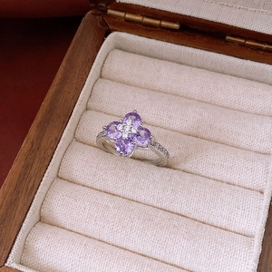 Macro shot of purple zircon four-leaf flower ring on a textured linen jewelry box