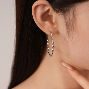 Close-up of a silver twisted geometric hoop earring worn by a model in a fashion shot