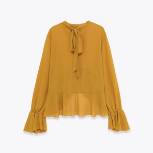Detail of mustard yellow chiffon blouse featuring bow tie neck and ruffled hem