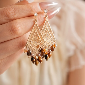 Ethnic gold diamond earrings with brown tiger eye beads shown in a handheld display