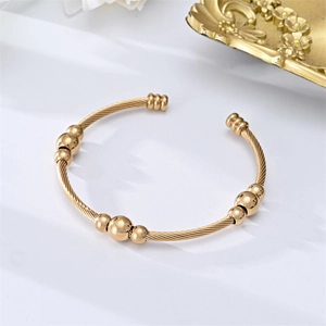 Adjustable gold stainless steel cable cuff bracelet with layered bead accents on white fabric