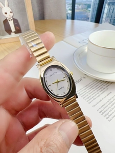 Close-up of a gold oval quartz watch with white dial being held in a lifestyle setting