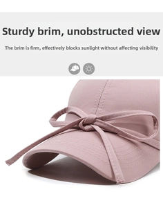 Detail showing the firm curved brim and pink ribbon bow on a cotton baseball cap