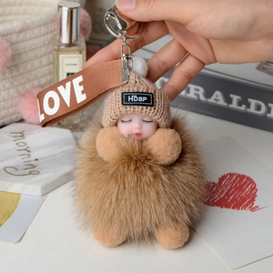 Detail of sleeping baby plush doll on fluffy brown fox fur pom pom with LOVE strap