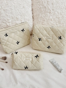 Three-piece set of cream quilted makeup bags featuring elegant black bow embroidery