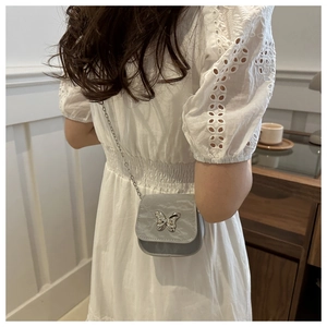 Detail showing the silver butterfly metal ornament and textured fabric of the grey saddle bag