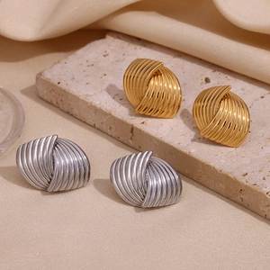 Macro shot of 18K gold and silver fan-shaped striped spiral earrings on beige silk fabric
