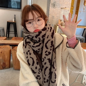 Close-up of a warm knit leopard print scarf styled on a model in a cozy cafe setting