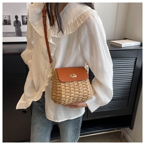 Detailed close-up of a brown woven straw crossbody bag featuring a golden metal lock