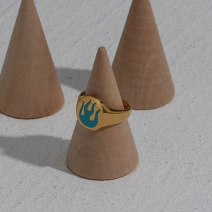Close-up of gold stainless steel ring with blue flame pattern on a wooden display stand