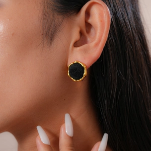 Close-up of black round stud earring with irregular gold trim worn by a model