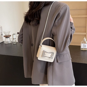 Mini cream crossbody bag with silver bow clasp and chain strap shown on a model