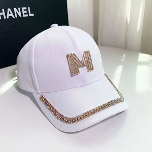 Detail shot of white cotton cap featuring a large golden M letter and colorful rhinestones
