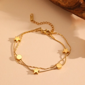 Gold double-layer snake chain bracelet with star and circle pendants on beige surface