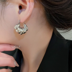 Close-up of a silver croissant-style hoop earring with a polished shell texture