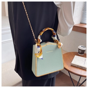 Close-up of mint green box bag with gold chain and silk scarf detail on handle
