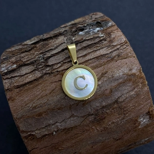 Natural shell round letter C pendant with gold plating on a rustic wood base