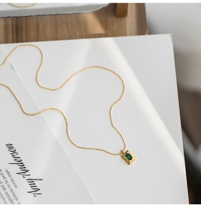 Detailed macro view of the gold chain and square pendant with an emerald green gemstone