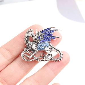 Macro shot of a silver dragon brooch with blue rhinestones held on a fingertip