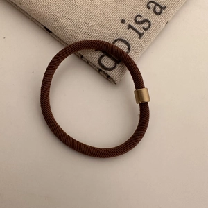 Detailed close-up of brown elastic hair tie with a matte gold metal buckle connector