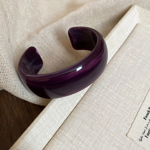 Detailed view of dark purple wide wavy resin bangle on a textured book surface