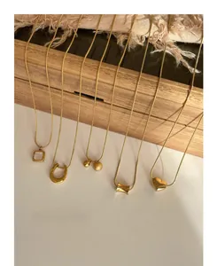 Detail of five gold titanium steel necklaces with shell and heart pendants on wood