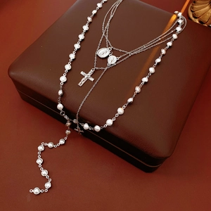 Detail of silver rosary necklace featuring a cross pendant and religious medals on pearls
