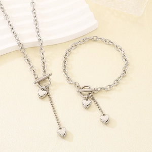Detail von silbernem Herz-Halsketten- und Armband-Set mit Knebelverschluss auf Texturfläche