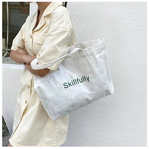 Detail shot of a large transparent tote bag with cream canvas and green Skillfully print