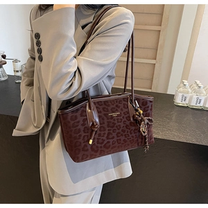 Détail d'un sac cabas léopard avec poignées en cuir brillant et pompon décoratif