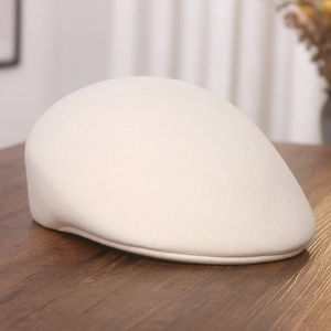 Detail view of a cream wool felt beret cap on a textured dark wood surface